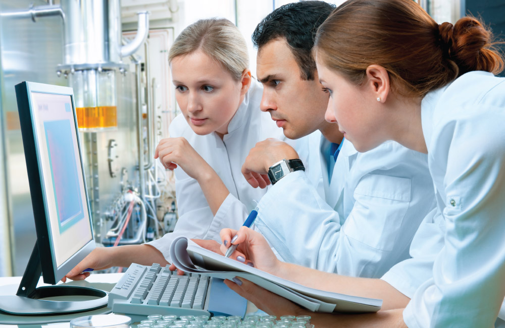 three scientists/doctors looking intently at a computer screen in a lab