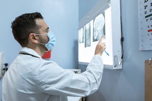 A masked doctor examining x-ray images of a patient’s neck and head