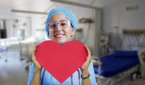 A professional healthcare worker holding up a large red paper heart