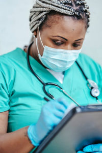 A masked healthcare professional making notes on a patient’s chart