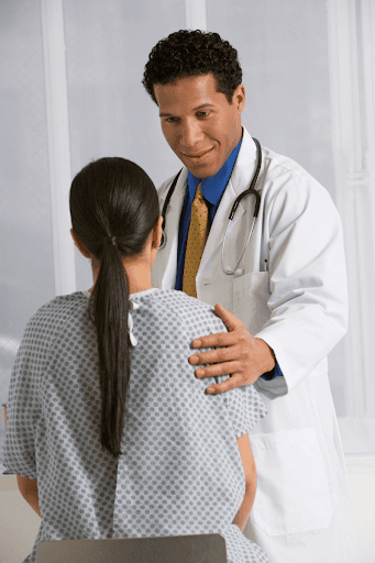 A doctor putting his hand on a female patient’s shoulder]